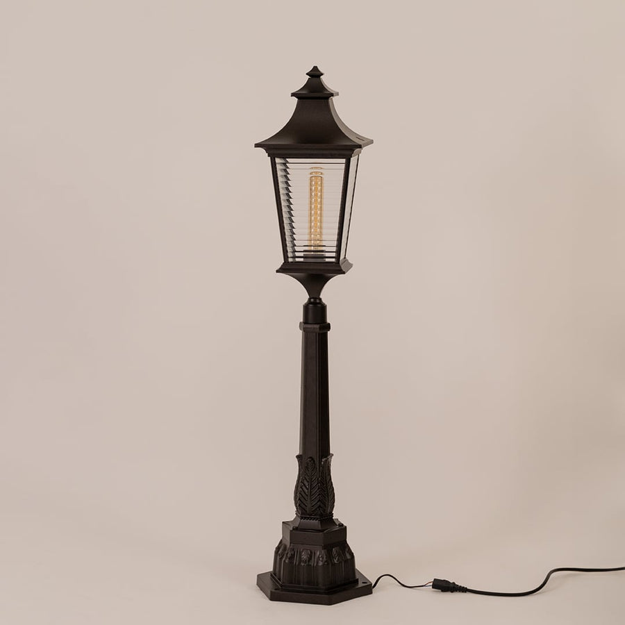 Black outdoor pillar lamp with clear ribbed glass and metal frame displayed on white background with bulb off.