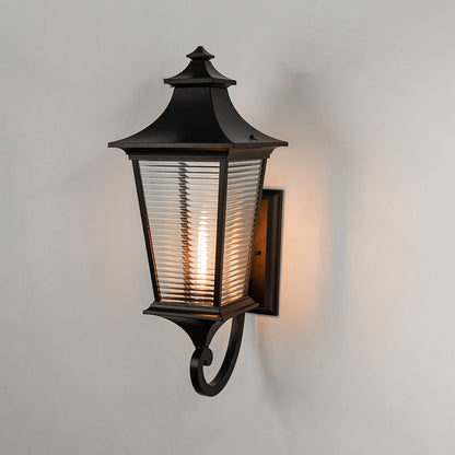 Black metal outdoor wall light on white background with horizontal ribbed glass shade illuminating warm patio decor.