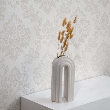 A modern arched ceramic vase holding dried grass stems displayed on a white surface against a patterned wallpaper backdrop creating elegant minimal botanical décor for interiors.