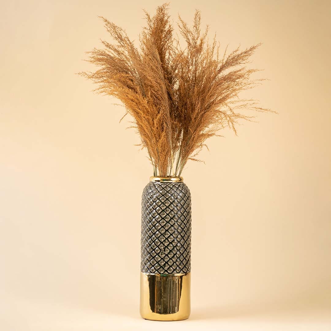 A tall textured grey and gold vase displayed with dried brown pampas on a soft beige background creating a warm lifestyle decor scene filled with natural elegance.