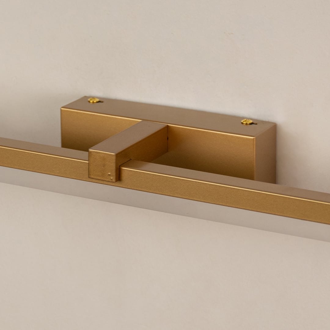 Closeup of gold metal picture light showing slim bar design smooth finish and warm directional illumination.
