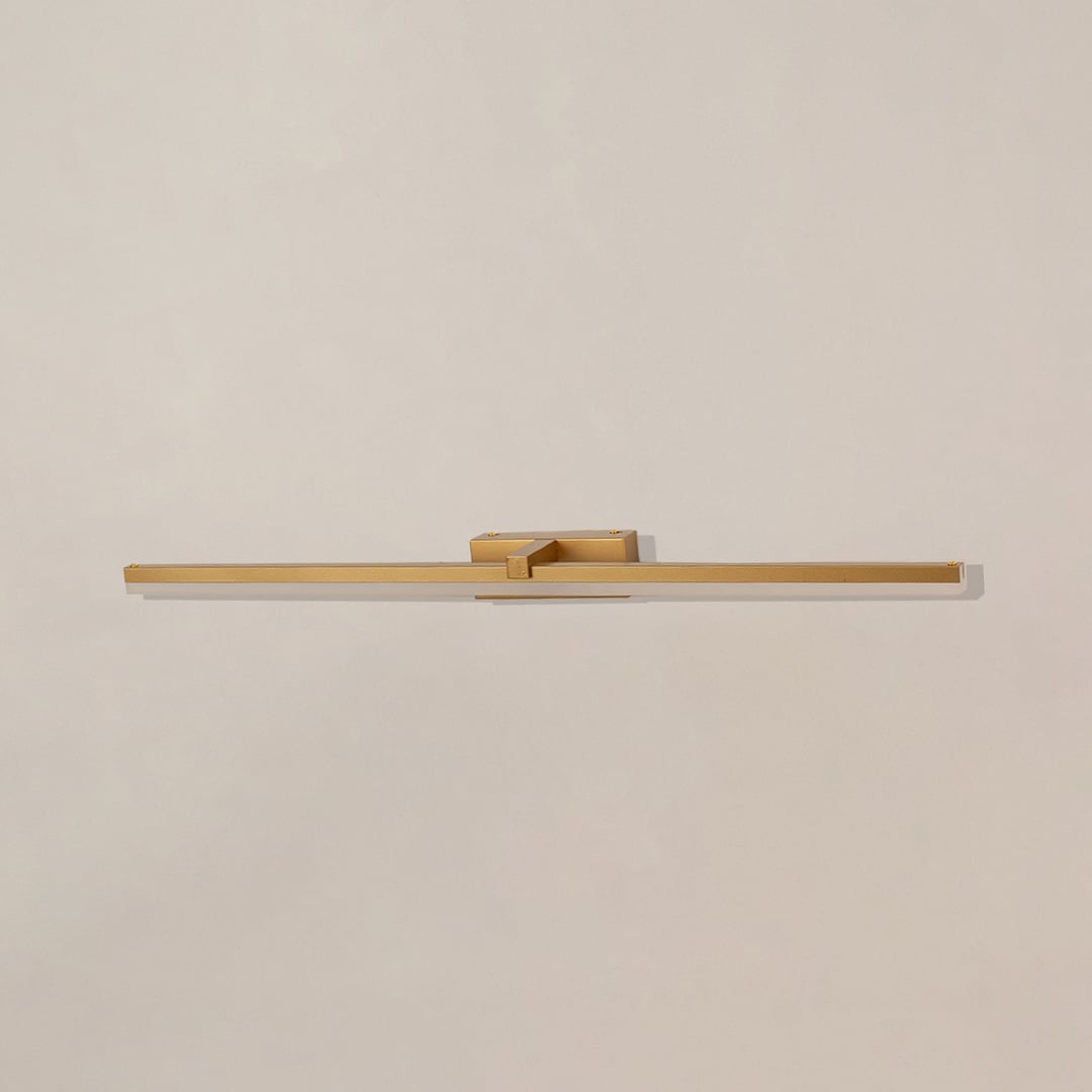 Gold metal picture light on a white background with the light off highlighting its minimal modern design.
