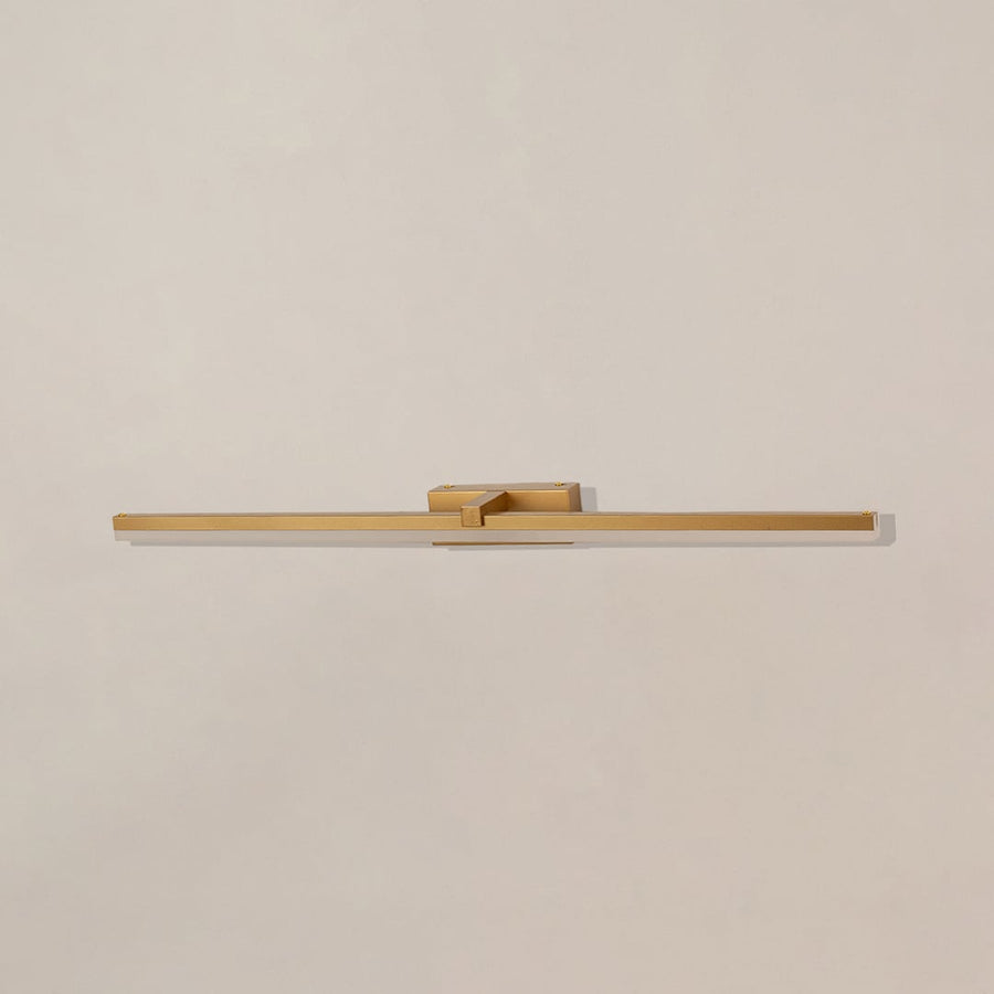 Gold metal picture light on a white background with the light off highlighting its minimal modern design.