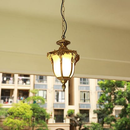 Black metal outdoor pendant light hanging on a porch ceiling with warm light on creating an inviting glow against a blurred building background.