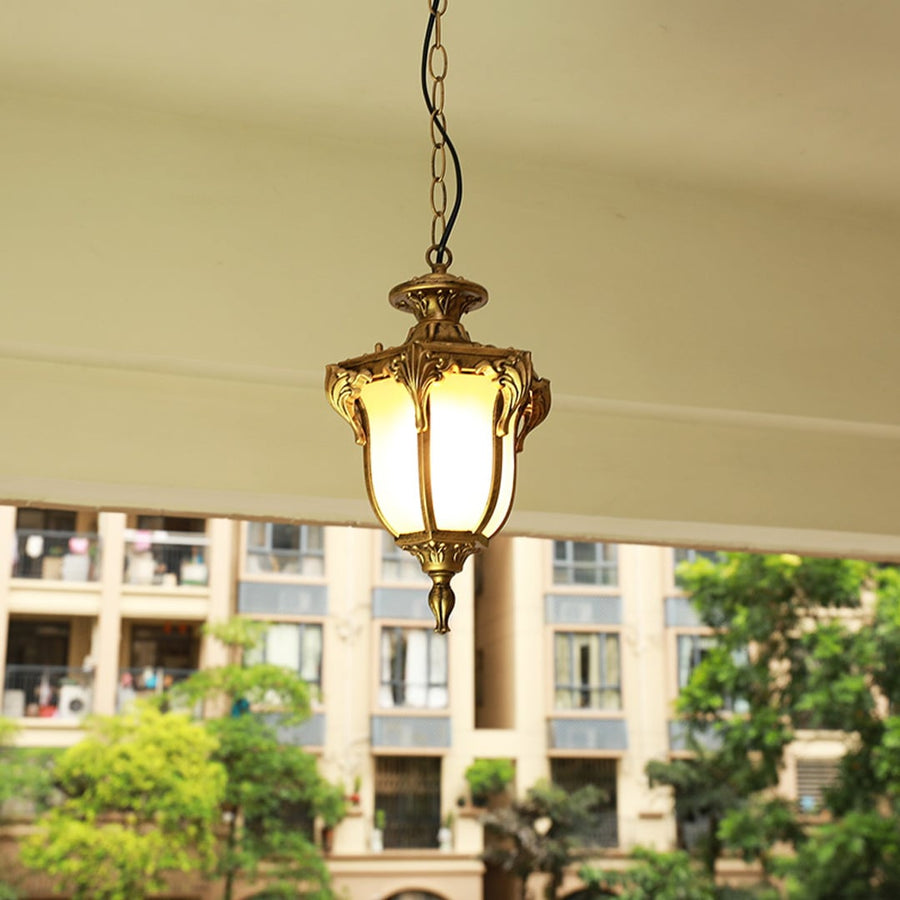 Black metal outdoor pendant light hanging on a porch ceiling with warm light on creating an inviting glow against a blurred building background.