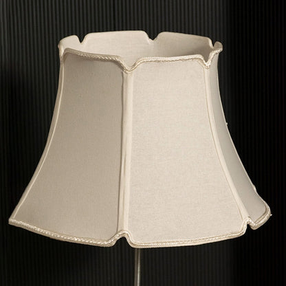 Elegant fabric lampshade displayed on a black background with the light turned off showing its soft scalloped edges and textured material in a warm neutral tone.