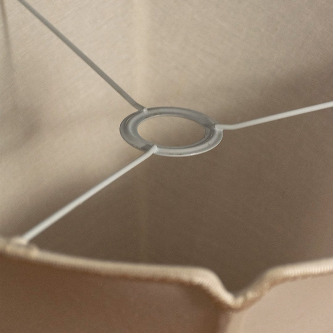 Closeup view of cream fabric lampshade with metal frame detailing showcasing handcrafted texture and elegant design.