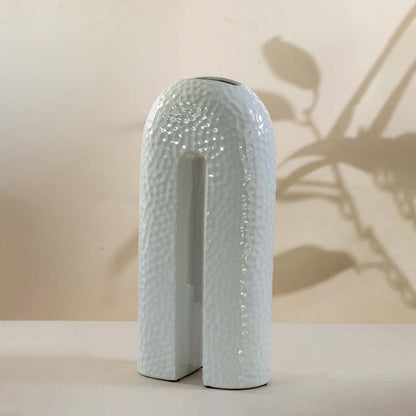 Modern white ceramic arch vase with glossy texture and hollow center shown on white background for home interiors.
