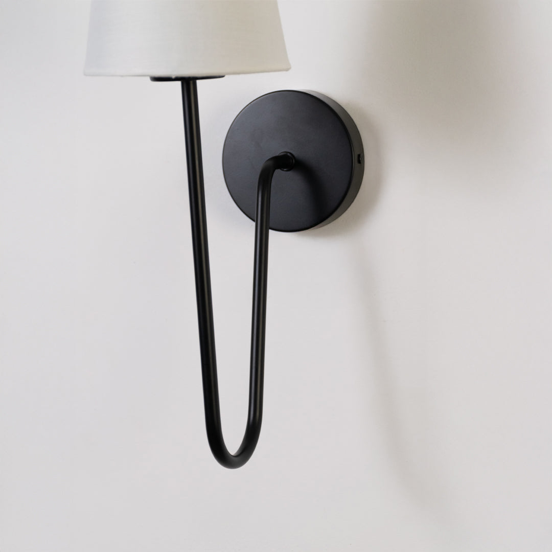 Minimal wall light in black metal finish with curved arm for bedroom or living room decor lighting white background.