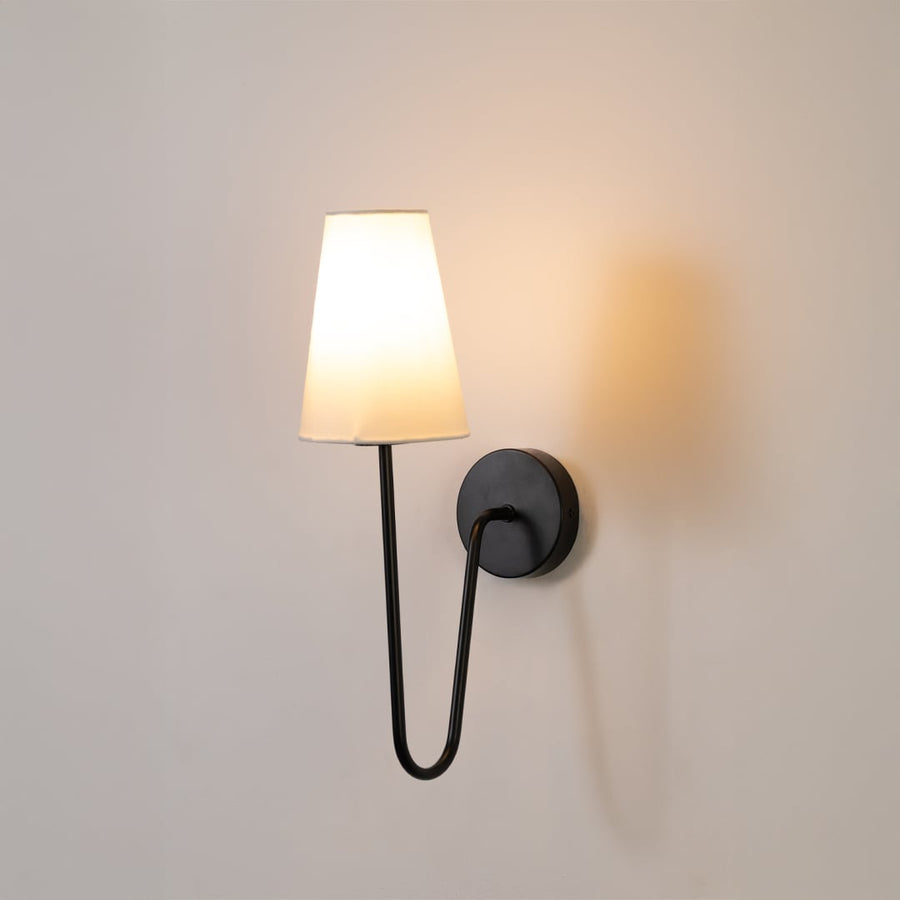 Black metal wall light with a tall white shade glowing softly on a clean white background adding modern style to bedroom or hallway decor.
