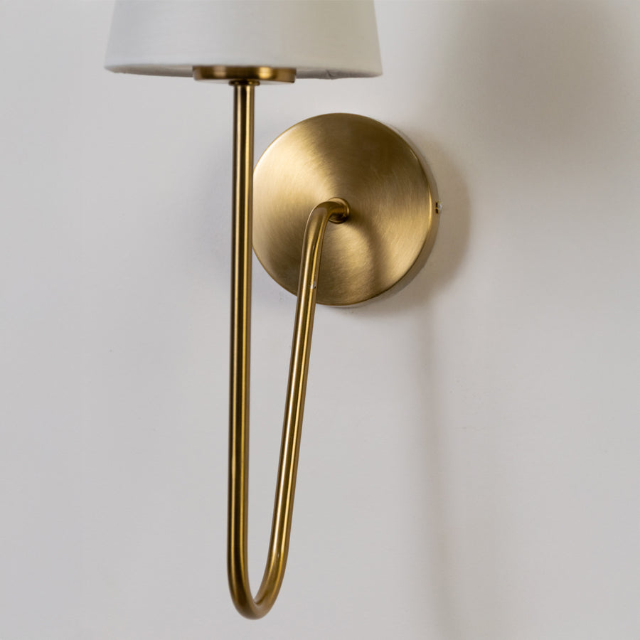 Modern wall light in gold metal finish with curved arm for bedroom or living decor lighting placement white background.