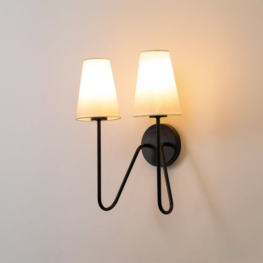 Black double wall light with two white shades glowing softly on a clean white background bringing a modern touch to home lighting decor.