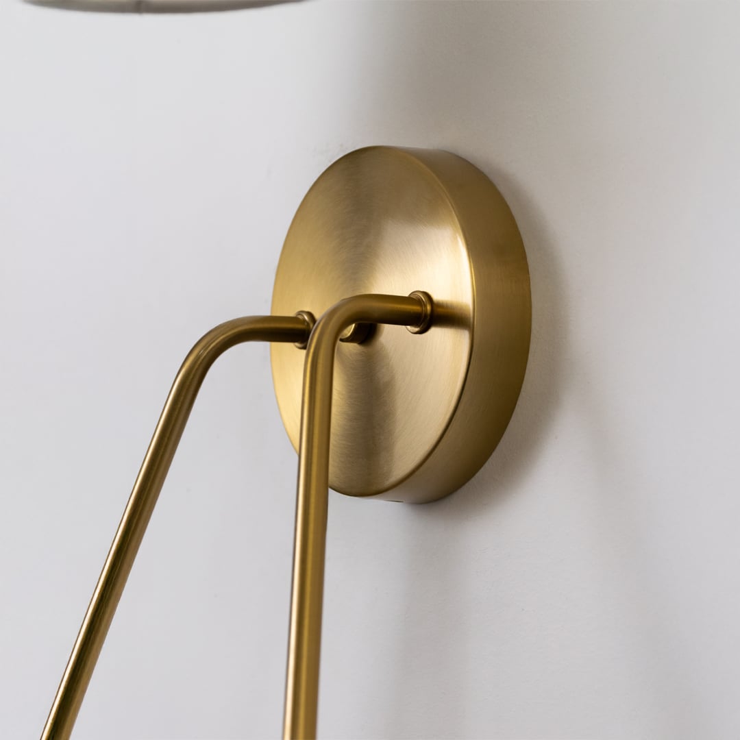 Closeup view of a gold double wall light with elegant curved arms and twin white shades showing premium detailing for home lighting.