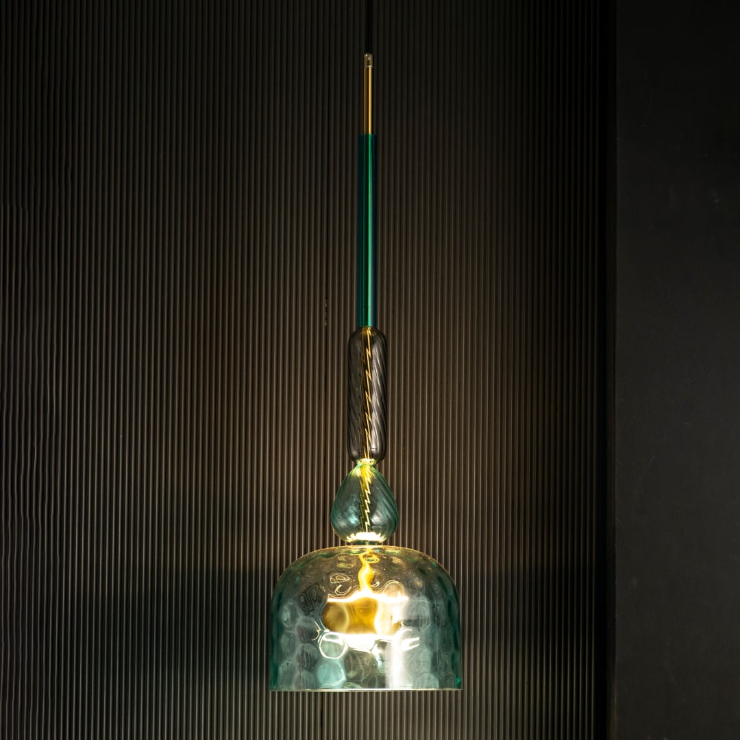 Rosetta teal glass pendant light glowing gently against a dark background highlighting its artistic glass texture.