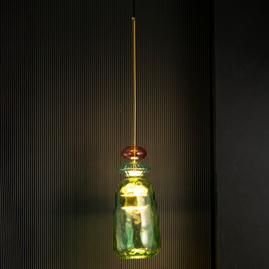 Rosetta green and pink glass pendant light glowing warmly against a dark background emphasizing its sculptural glass texture.