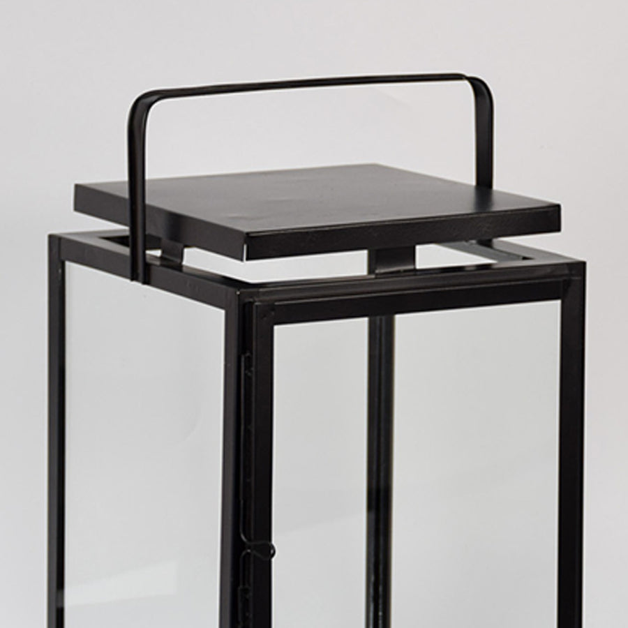 Closeup of black metal lantern with flat top handle for modern indoor decor styling use.