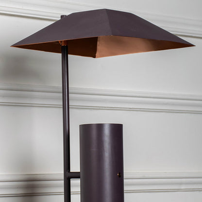 Closeup of dark brown metal table lamp showing geometric shade and cylindrical base for contemporary home lighting style.