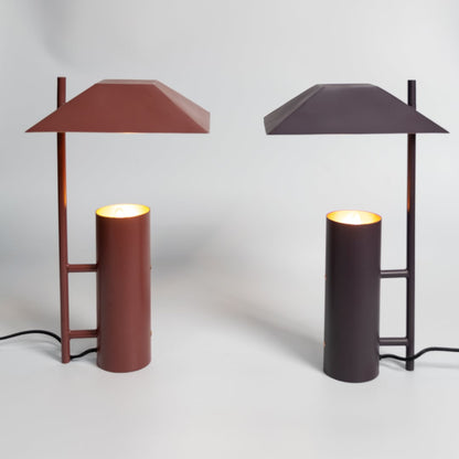 Dark brown metal table lamp with cylindrical base displayed in a styled setup for modern decorative tabletop lighting.
