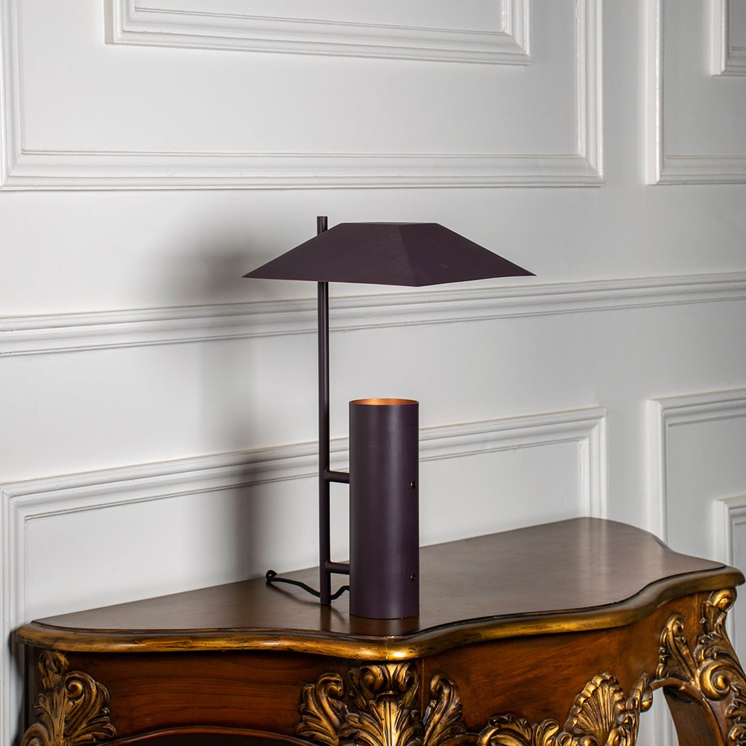 Dark brown metal table lamp with geometric shade glowing softly on white background for modern home lighting decor.