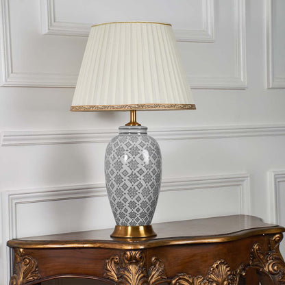 Grey ceramic table lamp with gold detailing and pleated shade displayed on a white background with the light turned off.