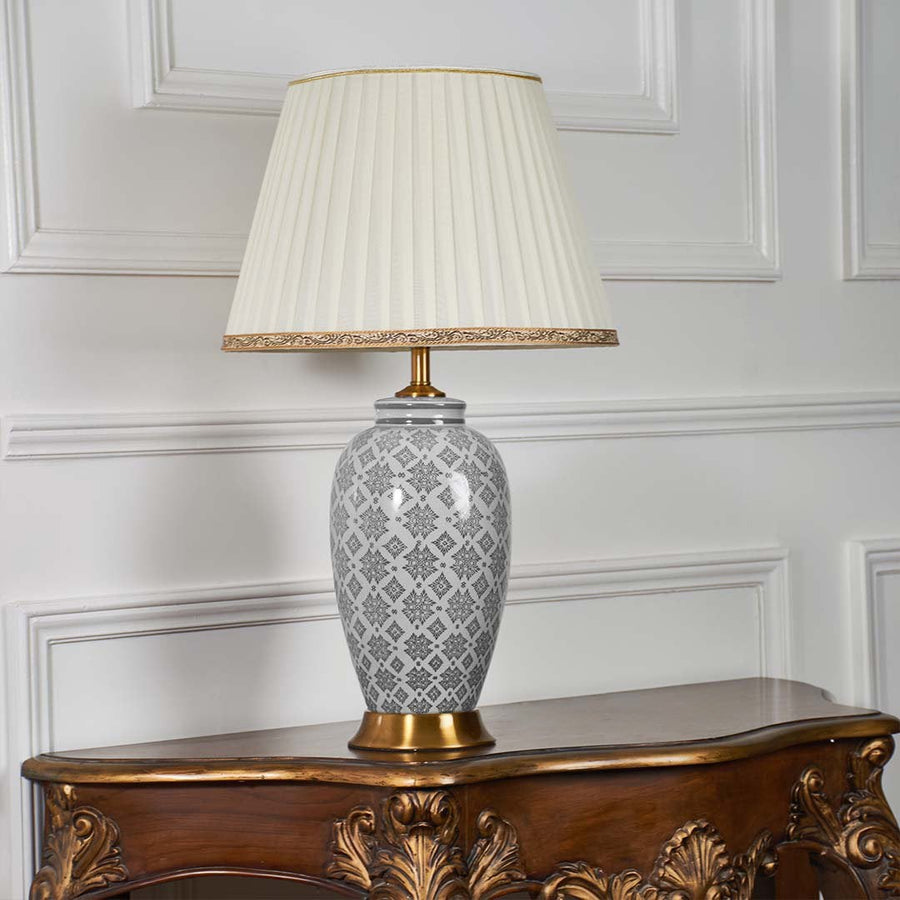 Grey ceramic table lamp with gold detailing and pleated shade displayed on a white background with the light turned off.