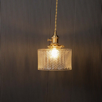 Clear textured glass pendant light glowing elegantly with brass holder against black background for stylish interiors.