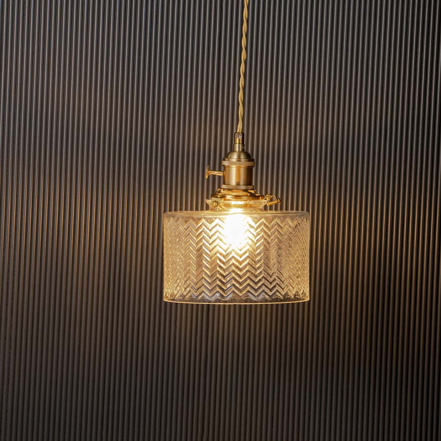 Clear textured glass pendant light glowing elegantly with brass holder against black background for stylish interiors.