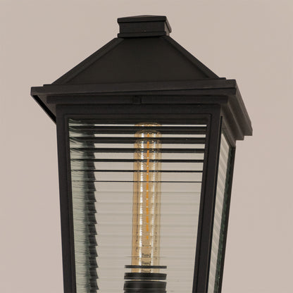 Closeup of black outdoor garden light with ribbed glass panels for elegant exterior decor styling use.