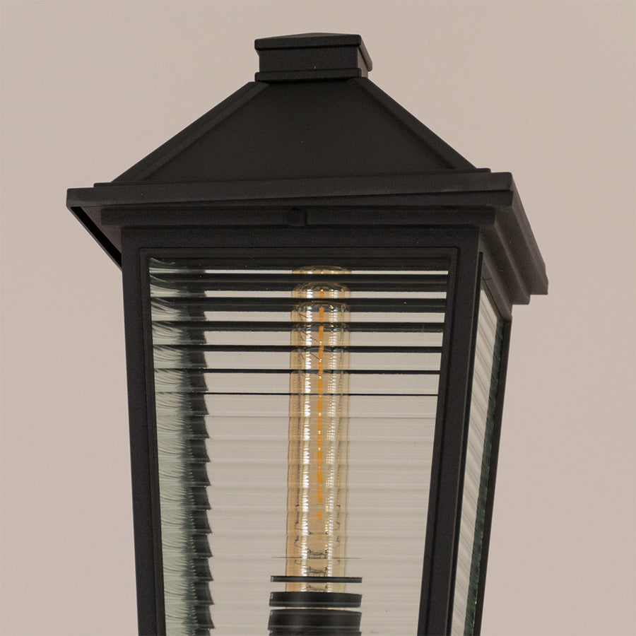 Closeup of black outdoor garden light with ribbed glass panels for elegant exterior decor styling use.