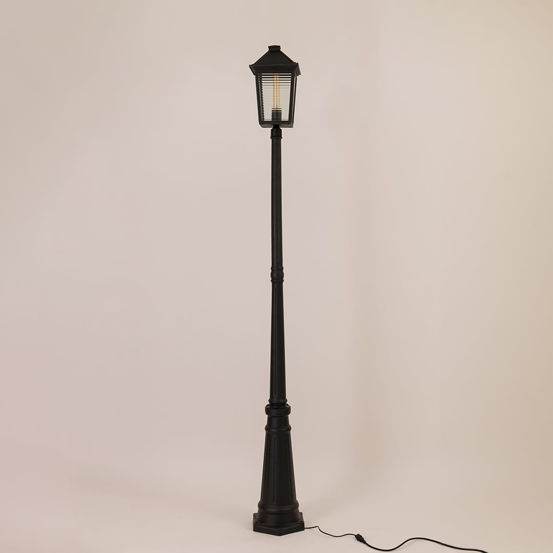 Classic black metal outdoor post light with lantern style head and tall decorative pole switched off on white backdrop.