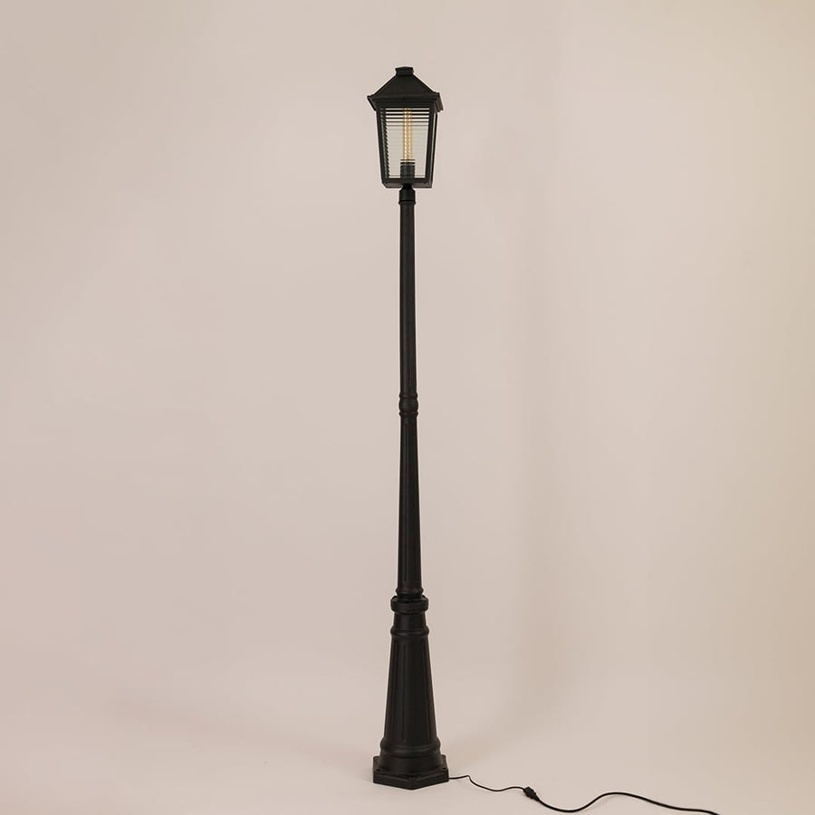 Classic black metal outdoor post light with lantern style head and tall decorative pole switched off on white backdrop.