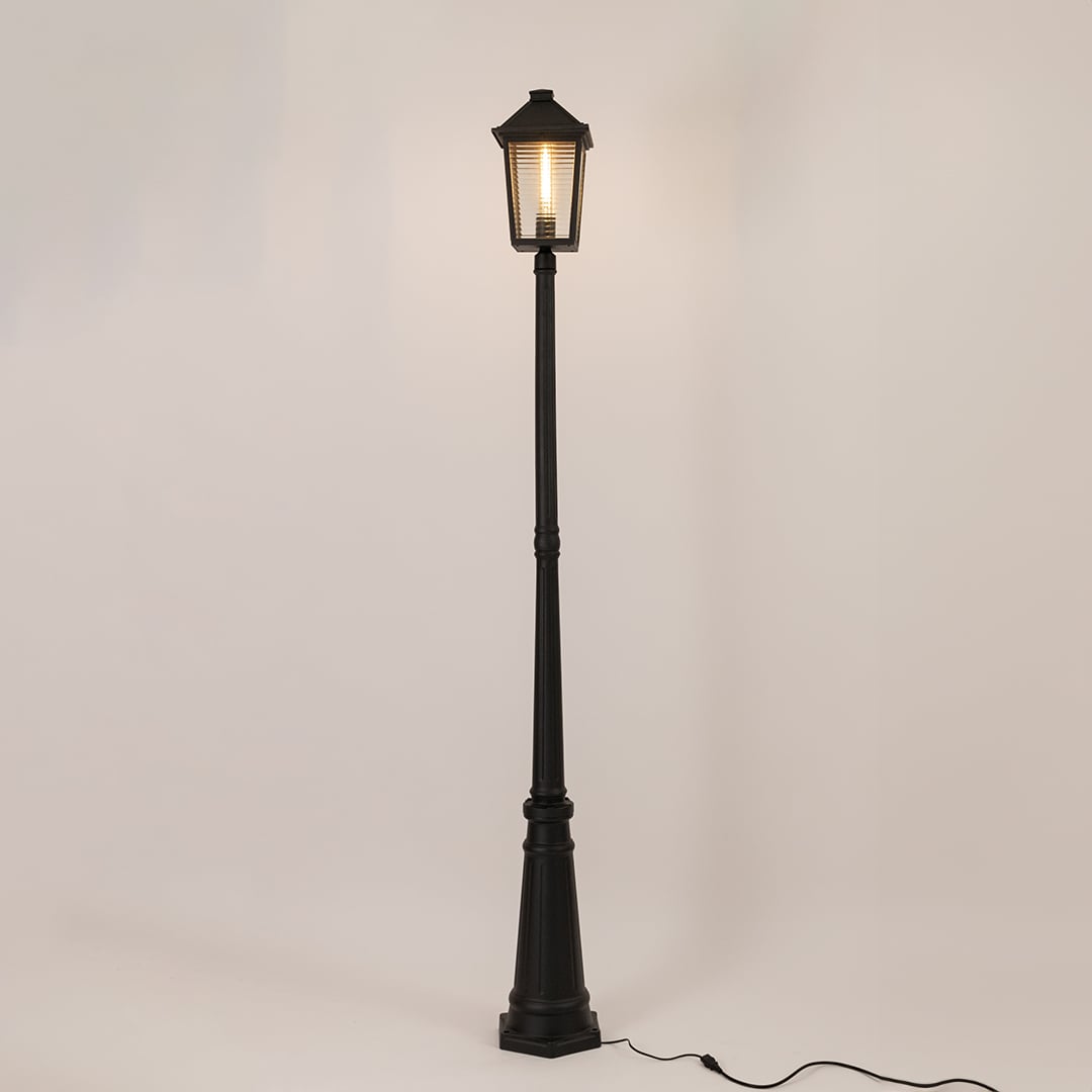 Illuminated black outdoor post lamp with glowing lantern head and textured glass panels on clean white background display.