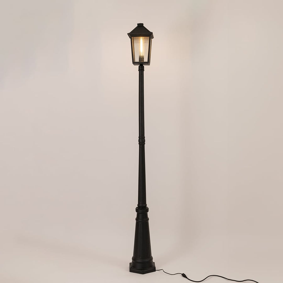 Illuminated black outdoor post lamp with glowing lantern head and textured glass panels on clean white background display.