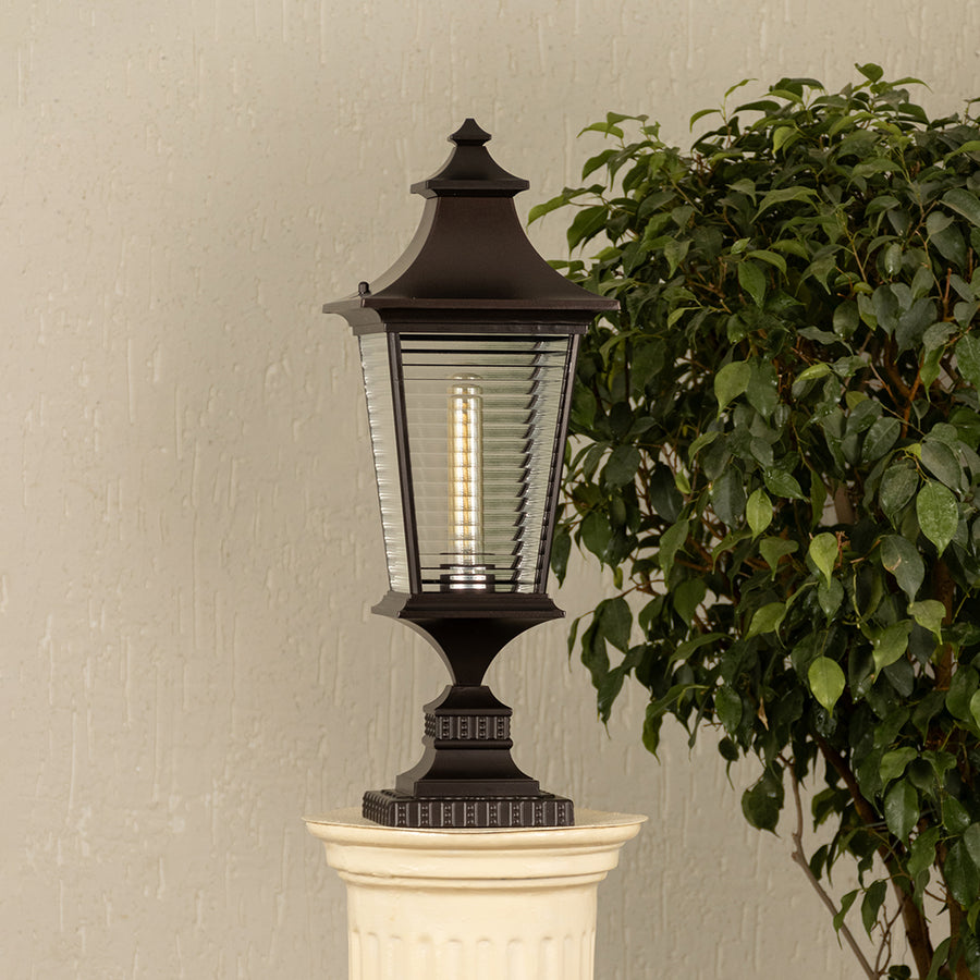 Black metal lantern with ribbed glass Light On placed next to a ficus plant Lifestyle image for patio decor.