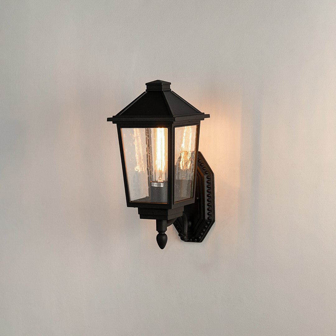 Black aluminum outdoor wall light on white background with clear tapered paneled glass shade for patio path decor.