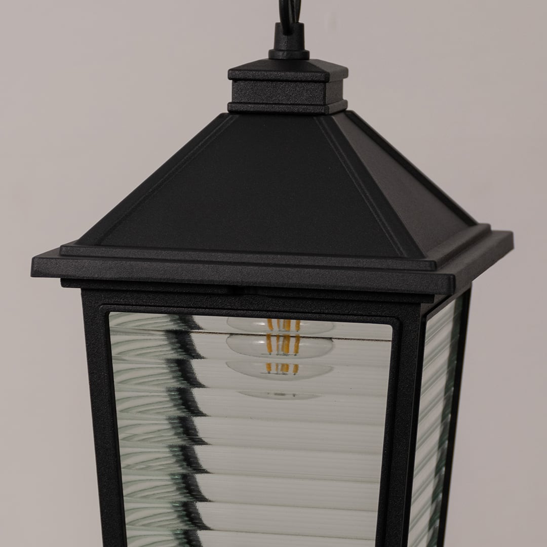 Close up view of black hanging lantern showing metal frame horizontal ribbed glass texture and vintage style bulb detail.