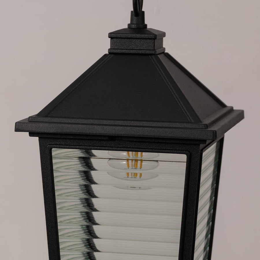 Close up view of black hanging lantern showing metal frame horizontal ribbed glass texture and vintage style bulb detail.