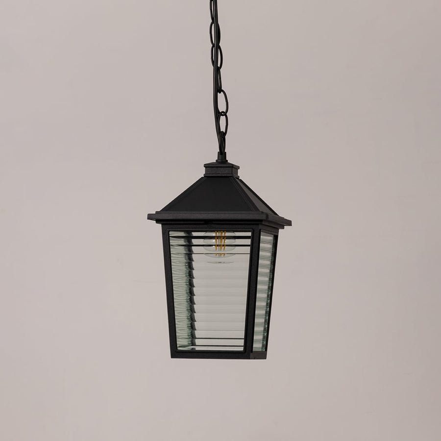 Classic black metal outdoor hanging light with textured glass and chain suspension switched off on minimal white backdrop.