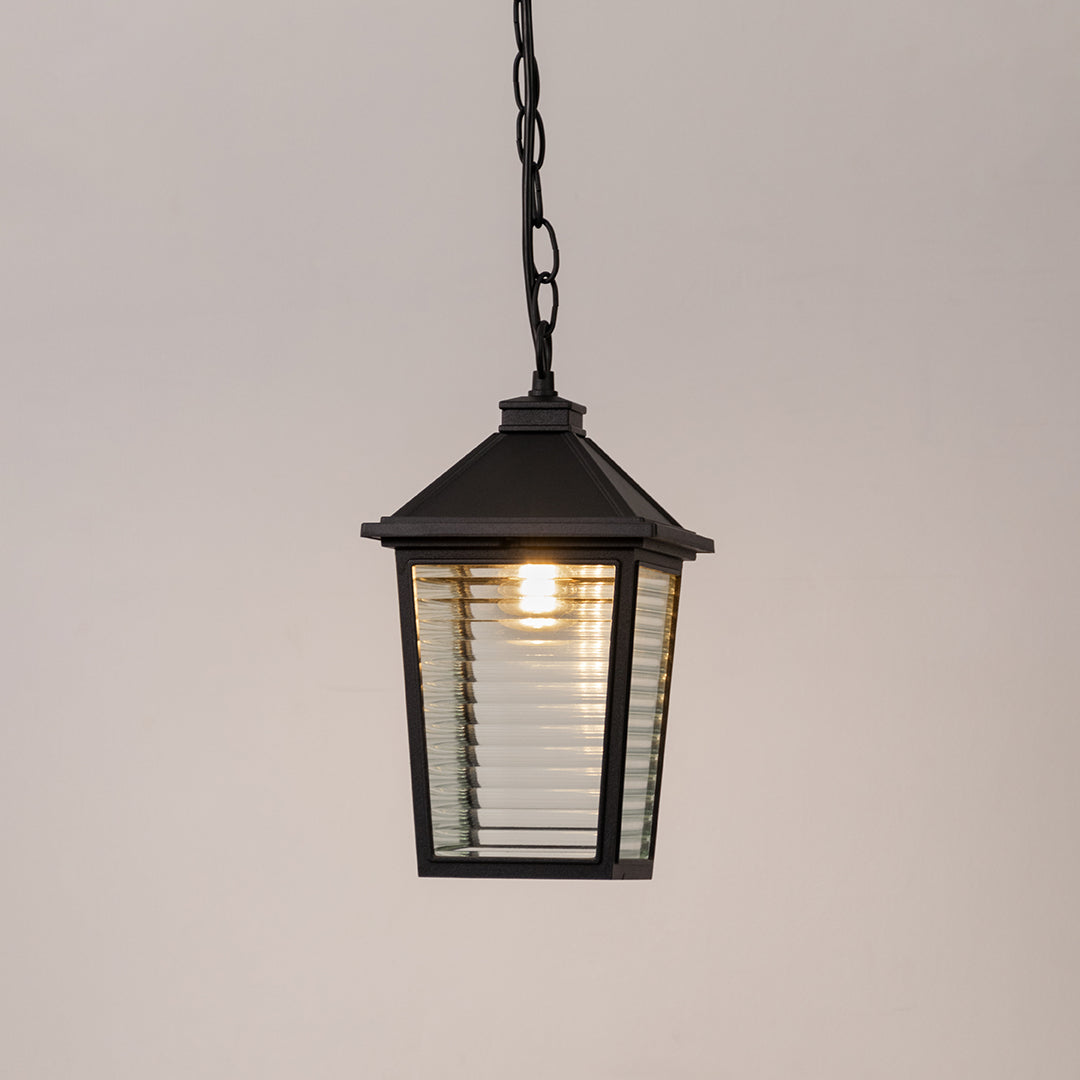 Contemporary outdoor pendant light in black metal with ribbed glass panels for entrance or patio decor lighting white background.