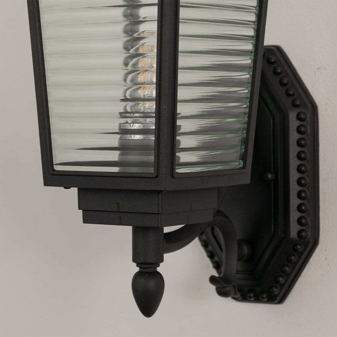 Close up view of black wall lantern showing horizontal ribbed glass detail metal frame and decorative mounting bracket design.