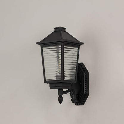 Traditional black metal wall lantern with textured glass panels and ornate bracket switched off on minimal white backdrop.