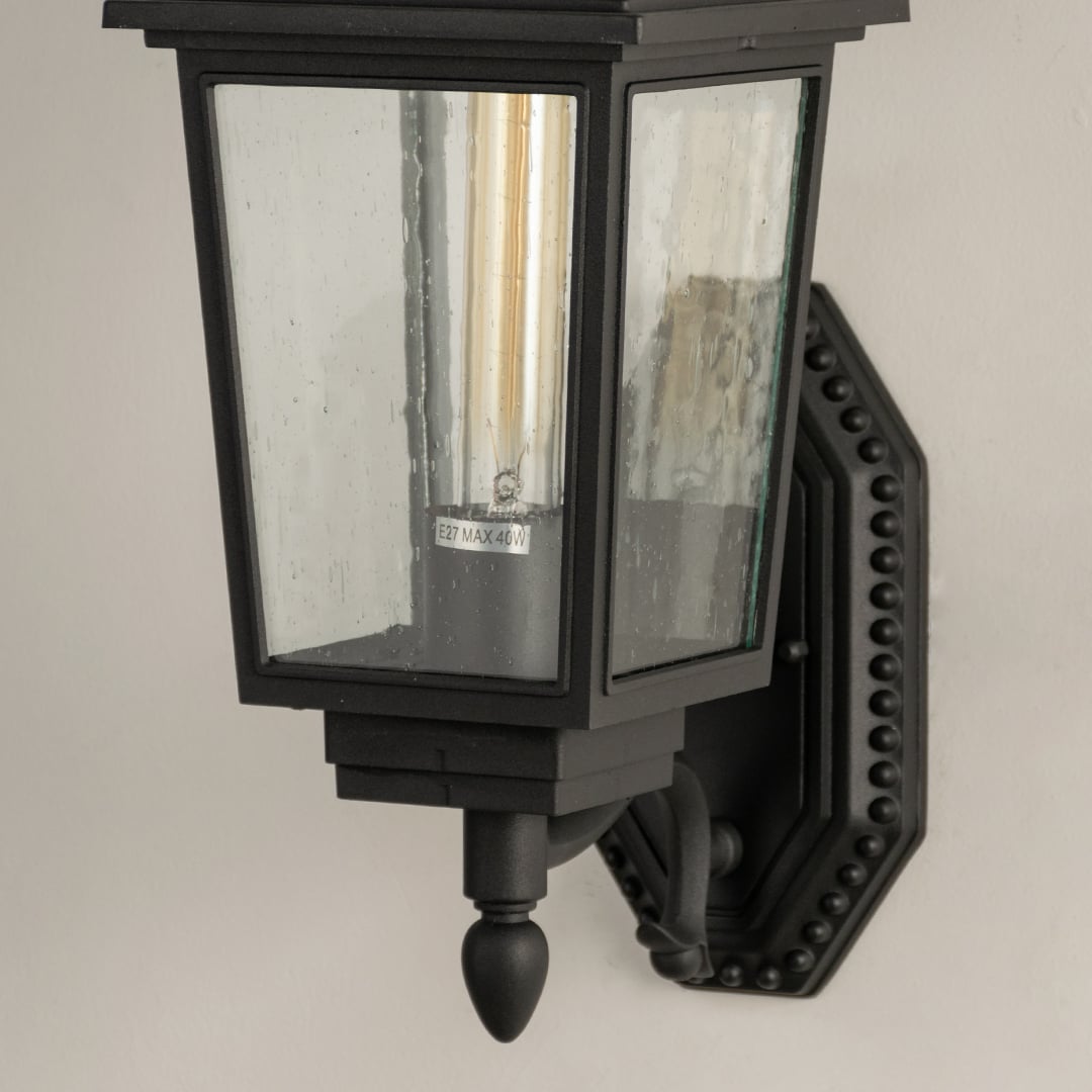 Closeup of black metal outdoor lantern showing clear textured glass panels and detailed vintage style frame for refined exterior lighting.