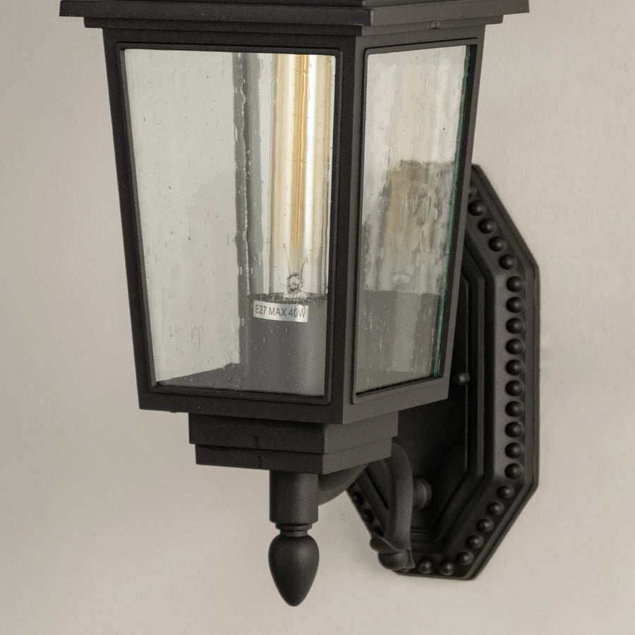 Closeup of black metal outdoor lantern showing clear textured glass panels and detailed vintage style frame for refined exterior lighting.
