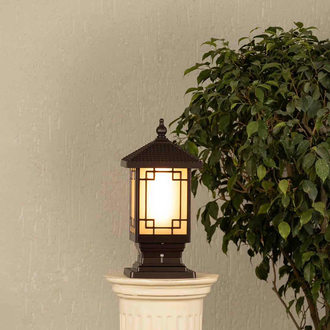 Black metal outdoor post lantern Light On mounted on a stone pillar Traditional garden gate lighting Main Lifestyle image at night.