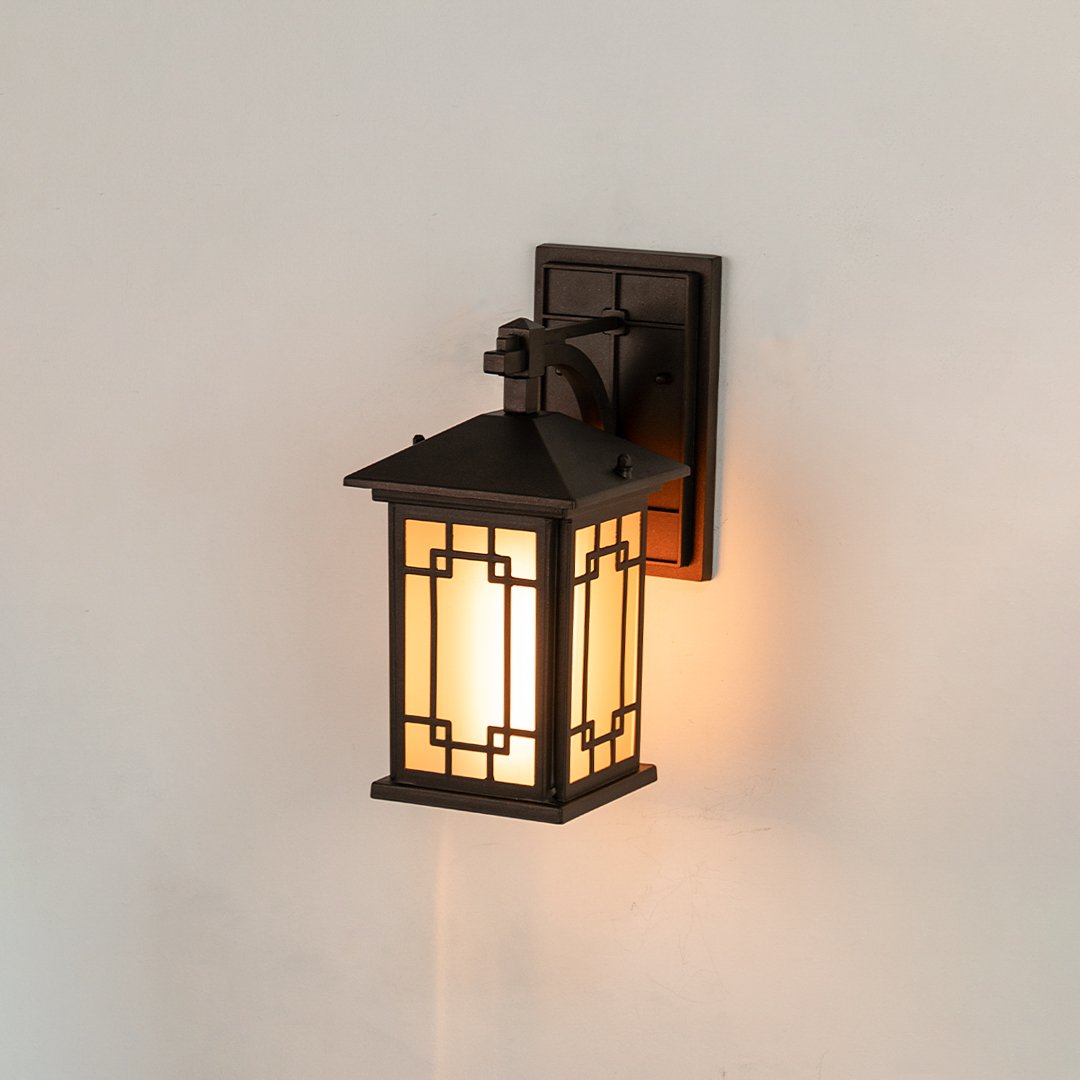 Black metal outdoor wall lantern on white background with an intricate geometric lattice frame and frosted glass panels.