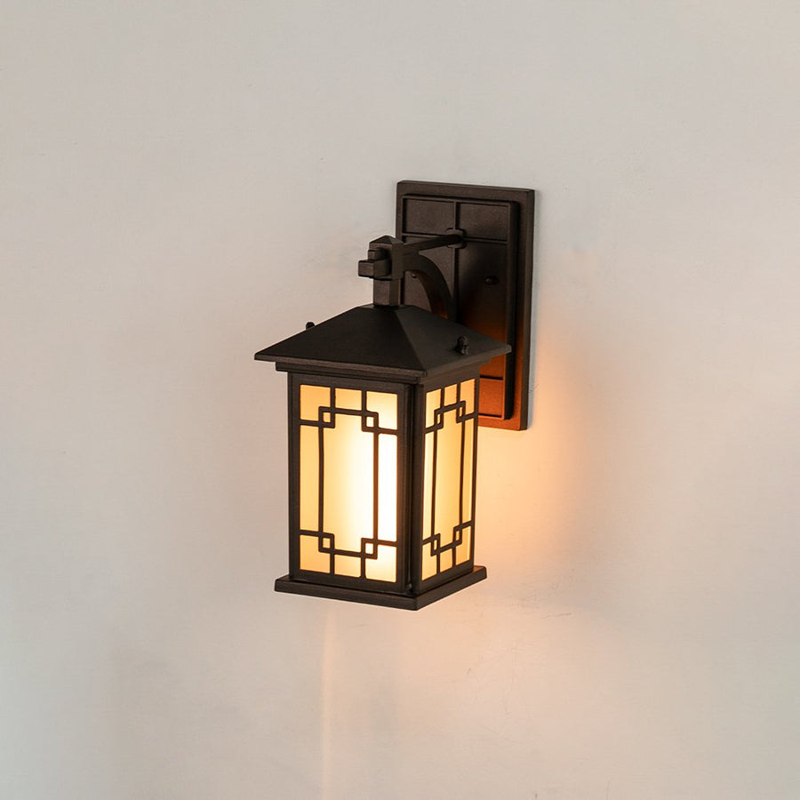 Black metal outdoor wall lantern on white background with an intricate geometric lattice frame and frosted glass panels.