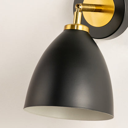 Closeup of black and gold metal wall light with smooth cone shade for luxury modern interior decor styling.