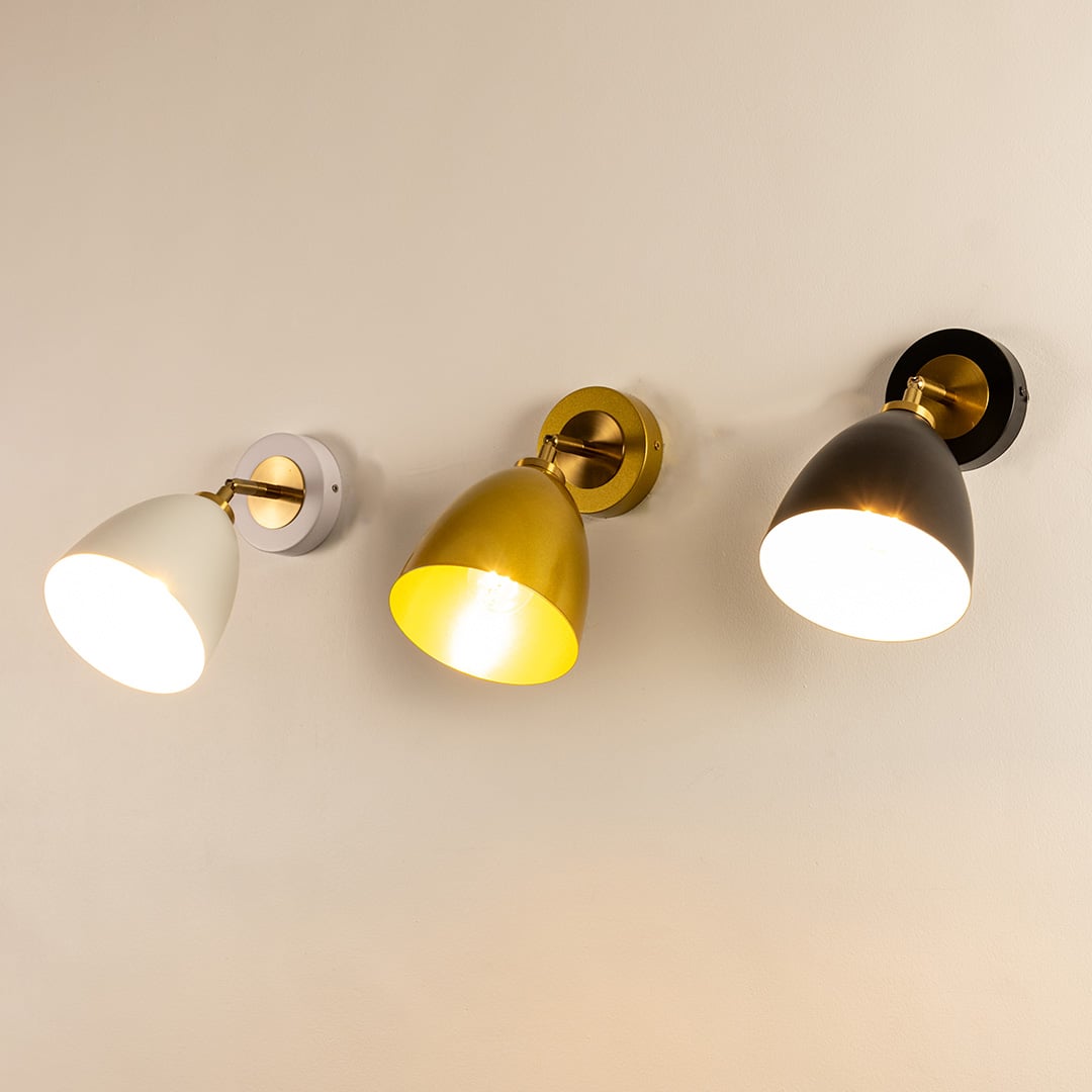 A trio of metal wall lights in white gold and black glowing warmly against a soft beige wall creating bright illumination and stylish contemporary sconce décor for modern interiors.