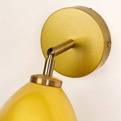 Closeup of yellow metal wall light mount and arm highlighting smooth finish solid construction and premium lighting craftsmanship.