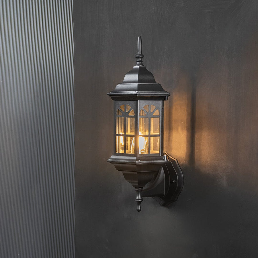 Black lantern wall light with warm bulb illumination highlighting the design on a dark background.